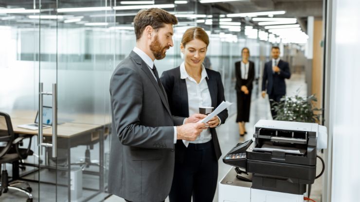 TTwo IT professionals reviewing documents beside an office printer, representing printer security and management.
